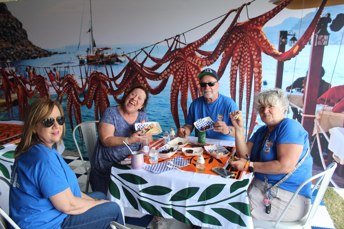 Guests laughing together over gyros at the 2023 Greek-themed House of Hogs booth