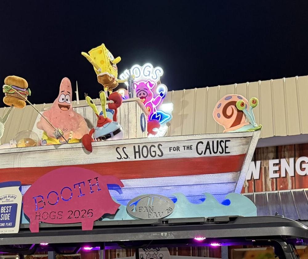 The Hogs on the Half Shell neon sign glowing at night on the S.S. Hogs for the Cause boat cart, surrounded by SpongeBob characters and a Best Booth 2026 pig plaque